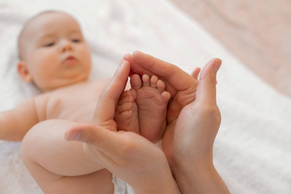 closeup of the bare feet of a newborn baby in his mother's hands on a white background